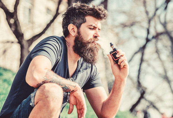 Бородатый человек курит вапе. Курение электронных сигарет. Курящее устройство. Мужчина с длинной бородой, расслабленный от курения. Человек с бородой выдыхает дым. Облака ароматизированного дыма. Концепция снятия напряжения