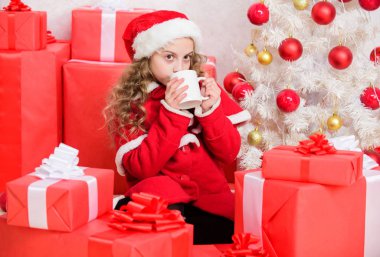 Çocuk Noel Baba şapkası sıcak içeceğin tadını çıkarıyor. Çocuklar için lezzetli sıcak içecekler. Küçük sevimli kız Noel 'i kutlarken elinde sıcak içecekle fincanı tutuyor. Noel arifesinde sıcak kakao içeceğim. Kakao en sevdiği içecek.