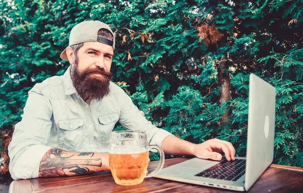 Laptop continues to assist virtual employees. Laptop user drinking beer in outdoor cafe. Bearded man working on laptop computer. Hipster using laptop with free internet access — Stock Photo, Image