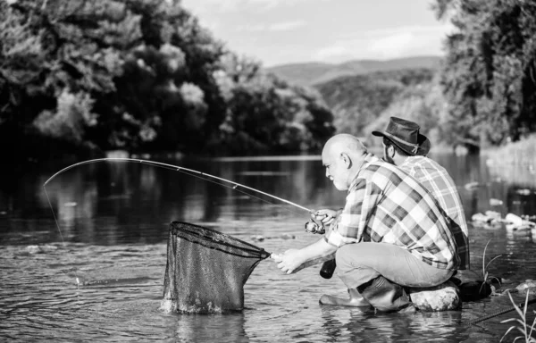 Beautiful evening riverside. Men riverside catching fish. Teaching fishing. Sharing his secrets. Transferring knowledge. Friends spend nice time at riverside. Experienced fisherman show tips to son — Stock Photo, Image