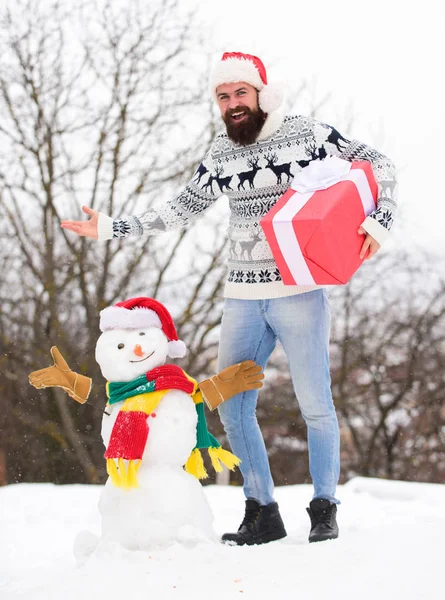 Los sueños se hacen realidad. hipster feliz listo para Navidad. vacaciones de invierno. suéter caliente en clima frío. hombre de santa dar regalo al aire libre. hombre barbudo construir muñeco de nieve. actividad de temporada de invierno. Feliz Navidad. — Foto de Stock