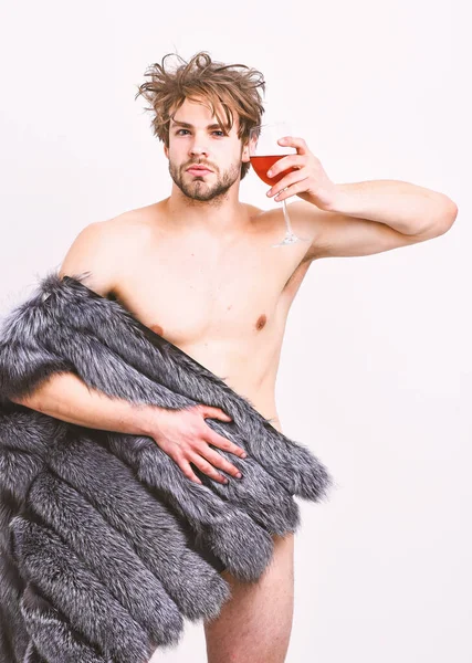 Chico atractivo rico posando abrigo de piel en cuerpo desnudo. Moda y pathos. Atleta rico disfrutar de su vida. Riqueza y concepto de lujo. Sexy soñoliento rico macho tousled pelo beber vino aislado en blanco — Foto de Stock