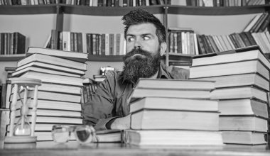 Katı yüz sit Kitaplığı'nda, eğitim sırasında kitaplar, kitap rafı arka plan üzerinde yığınları arasında adam. Kitap kurdu kavramı. Öğretmen veya tablo ile kum saati ve defocused gözlük, sakal oturup ile öğrenci