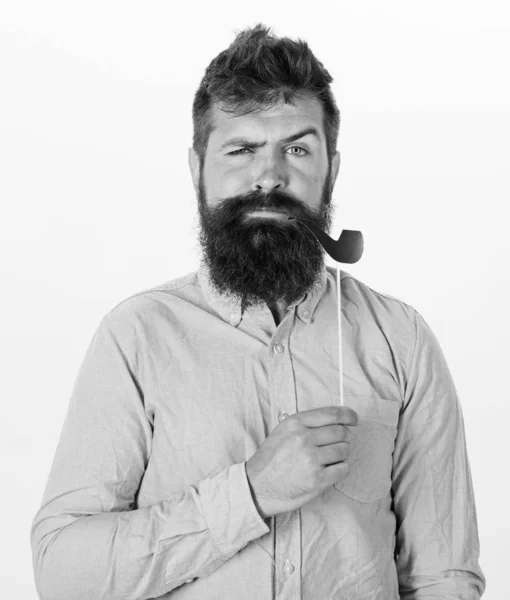 Conceito de hábitos antigos. Homem segurando papel partido adereços cachimbo de tabaco, fundo branco. Hipster com barba e bigode em rosto estrito posando com adereços de cabine de fotos. Guy fuma cachimbo de tabaco — Fotografia de Stock