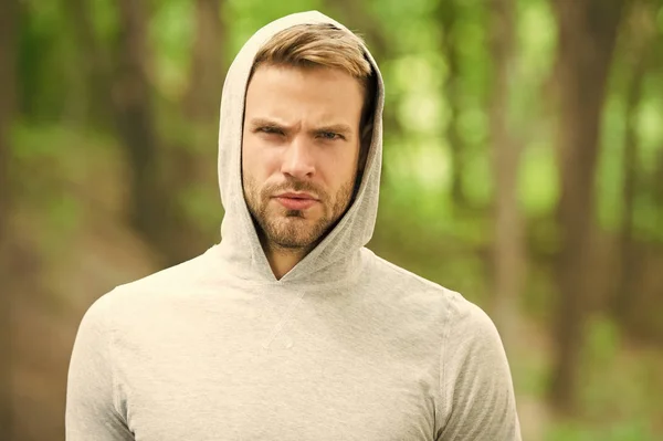 macho man. man in hood. casual style. male fashion. unshaven guy outdoor. seriousness and masculinity. sportswear fashion. sportsman relax after training outdoor. handsome unshaven man in hood