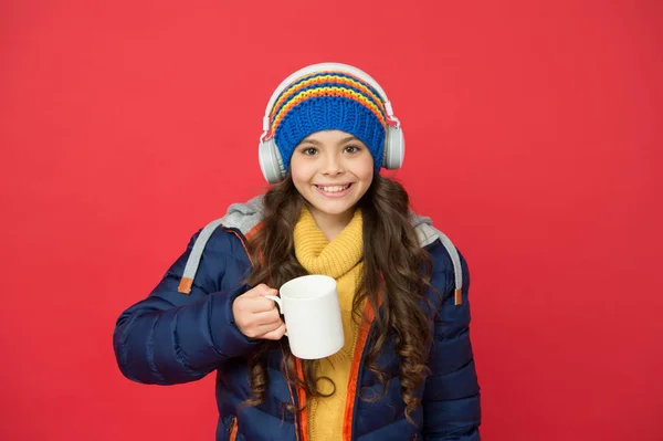 Ηρέμησε και πιες ζεστό γάλα. Ευτυχισμένο κορίτσι με κόκκινη κούπα γάλακτος. Μικρό παιδί απολαμβάνει τη μουσική και το τσάι γάλα. Σύγχρονη ζωή. Χειμερινές ή φθινοπωρινές διακοπές Το μόνο που χρειάζεσαι είναι γάλα και μουσική — Φωτογραφία Αρχείου