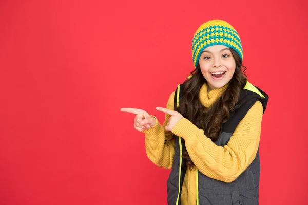 Qué bueno eso. Chica feliz señalando dedos índice fondo rojo. Niño pequeño en estilo invernal apuntando a algo. Señalando y promoviendo. Señalando el gesto. Para publicidad, espacio de copia —  Fotos de Stock