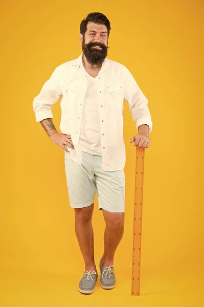 Terug naar de les is hier. Gelukkig hipster houden liniaal op gele achtergrond. Brutale hipster glimlachend voor wiskunde en geometrie les. Bearded Man in trendy hipster stijl. Beardy hipster op 1 september — Stockfoto