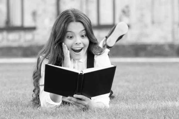 Bok med oväntad överraskning. Överraskad barn läsa bok om grönt gräs. Liten flicka läser med överraskande känslor i ansiktet. Söt liten skolflicka hålla mun öppnas av stor överraskning. Överraskning koncept — Stockfoto