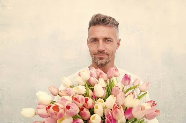 幸せな女性の日。特別な人のために。チューリップの花束を持つ男。ピンクの花を持っているハンサムな男。花を持つ魅力的な男。男はバレンタインデーや誕生日のお祝いのための贈り物を運ぶ。花屋 — ストック写真