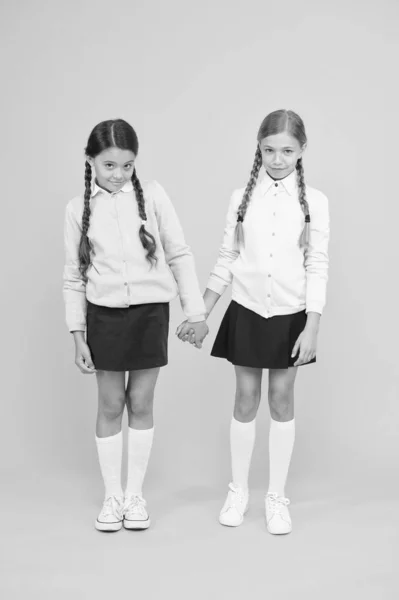 Feeling shy. Cute children holding hands on yellow background. Little children wearing school uniform. School children with fashion look. Small children with plaited hair are back to school — Stock Photo, Image