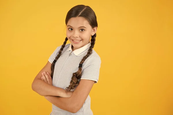 Confident in her knowledge. School lesson. Inspiration for study. Back to school. Knowledge day. Schoolgirl enjoy study. Kid school uniform. Smiling cutie crossed hands yellow background copy space — Stock Photo, Image