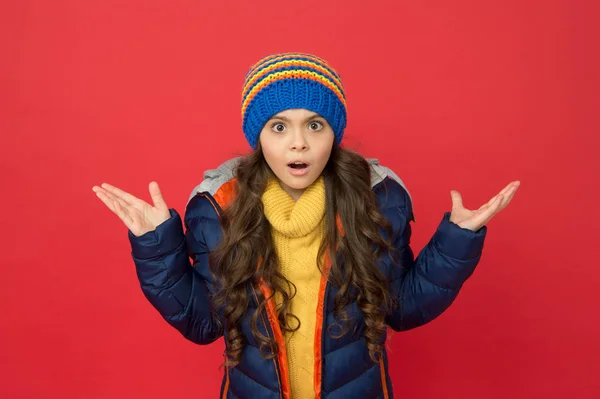 Konečně přichází zima. sezónní móda pro děti. malé krása červené pozadí. Holčičí nafoukaná bunda a pletený klobouk. starat se o sebe v chladném počasí. překvapené dítě v teplých zimních šatech — Stock fotografie