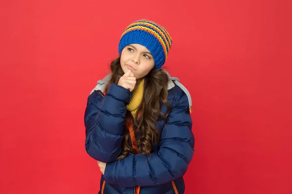 Sonho de inverno. criança pensativa em roupas quentes de inverno. moda sazonal para crianças. pequeno fundo vermelho beleza. jaqueta puffer menina e chapéu de malha. cuidar de si mesmo no tempo frio — Fotografia de Stock