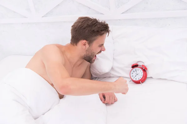 man angry because alarm rings. Angry man lying in bed early in morning. stop ringing. Sleep longer. Health care concept. male awake unhappy with alarm clock. Hateful schedule. Hardest moment of day
