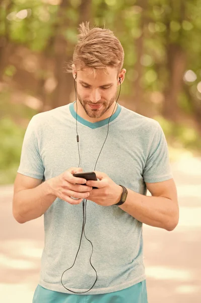 Pairing his fitness watch with his smartphone. Sportsman using fitness tracker for training outdoor. Fit man tracking his fitness activity with sports watch. Monitoring his health with fitness device