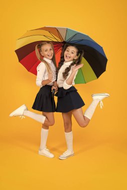 İlkokul modası. Renkli şemsiye tutan moda bakmak ile Mutlu okul çocuklar. Resmi üniformalı moda küçük kızlar sarı arka planda gülümsüyor. Küçük çocuklar için okul modası