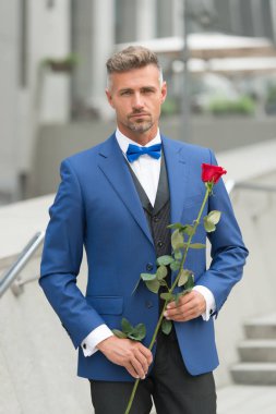 Yakışıklı erkek arkadaş kırmızı gül tutuyor. İşadamı kırmızı gül tutuyor. Zarif ve kendine güvenen bir adam. Klasik ceketli damat. Karizmatik bir adam gelinlik giyer. Tiyatro ve Opera. Randevu için restorana gidiyorum.