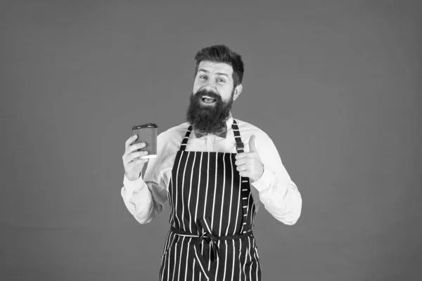 Bästa smaken någonsin. elegant självsäker bartender. Man dricker kaffe. Skäggig man håller ta bort kaffe. brutal servitör på caféet. mogen man röd bakgrund. skicklig tjänare. barista hipster kock förkläde — Stockfoto