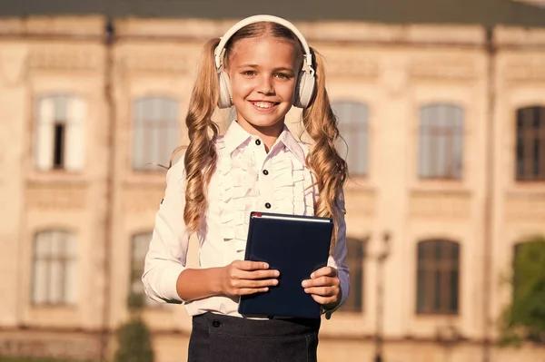 Słuchanie książki szkolnej. Technologie cyfrowe do nauki. ELearning i nowoczesne metody. Dziewczyna Cute uczennica trzymać książkę i słuchawki. Wiedza lepiej przyswajać w ten sposób. Koncepcja książek audio — Zdjęcie stockowe