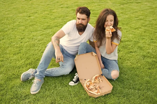 Simple happiness. Cheat meal. Couple eating pizza relaxing on green lawn. Fast food delivery. Bearded man and girlfriend enjoy cheesy pizza. Couple in love dating outdoors with pizza. Hungry people