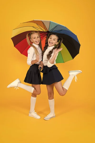 La moda della scuola elementare. Felice scuola bambini con look di moda in possesso di ombrello colorato. Moda ragazze piccole in uniformi formali sorridenti su sfondo giallo. Moda scuola per bambini piccoli — Foto Stock