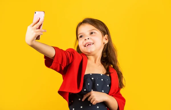 Hora da selfie. Menina pequena tirar selfie com fundo amarelo smartphone. Pequena câmera selfie criança no telefone móvel. Desfrutando de sessão de selfie em estilo de moda. Comunicação online. Rede social — Fotografia de Stock