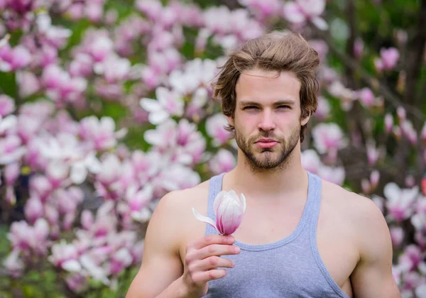 Mennesket blomster baggrund defokuserede. Botanisk natur. Mandlig skønhed. Hipster nyde blomstre aroma. Forårsskønhed. Frisure styling. Hårpleje og skønhed. Ubarberet mand magnolia blomstre. Smuk frisure - Stock-foto