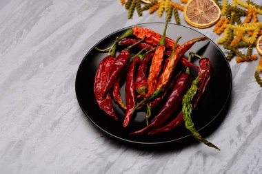 Kırmızı biber ve siyah seramik tabak içinde makarna ve malzemeler.