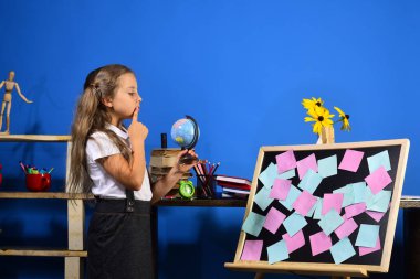 Düşünceli yüz ile kız öğrenci sınıfta dünya modeli tutar