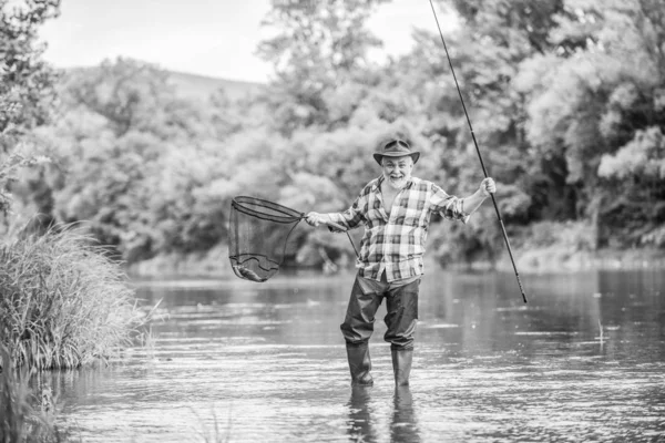 F per la pesca. hobby e attività sportive. Pothunter. pescatore con canna da pesca. uomo maturo pesca a mosca. uomo cattura il pesce. Pescatore barbuto in pensione. Esche di trota. weekend estivo. Grande gioco di pesca — Foto Stock