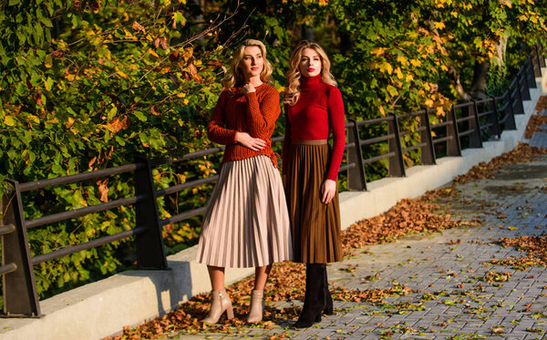 Осенняя мода. Плиссированная мода на юбки. Женщины гуляют в осеннем парке. Осенний стильный наряд. Очаровательные дамы наслаждаются солнечным осенним днем. Модная одежда. Женственность и нежность. Друзья девушки