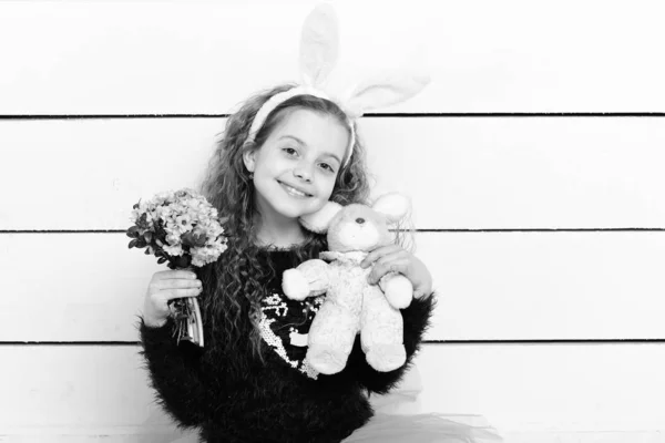 Chica feliz en orejas de conejo con juguete de conejo de Pascua, flores — Foto de Stock