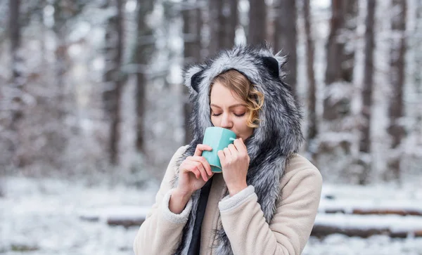 Las mejores vacaciones. caliéntese. Bebida de invierno mujer. Chica disfrutar del vino caliente. Mujer con sombrero bebiendo té en el bosque. sombrero de animal de piel hembra divertida. senderismo y viajes. chica excursionista beber taza de café caliente —  Fotos de Stock