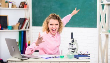 Masasında dizüstü bilgisayarı ve okul gereçleri olan bir kadın öğretmen ya da öğrenci. Sınıfın yazı tahtası geçmişinde duygusal kadın öğretmen eğitmeni. Duygusal kontrol için. Duygusal insanlar konsepti