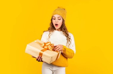 Çocuk hediyesini açarken heyecanlanıyor. Kızım için Noel hediyesi. Sürprizlerin. Küçük kız, sarı arka planda kurdelesi olan hediye kutusunu tutuyor. Genç kız tatil hediyesi aldı. En iyi Noel hediyeleri.