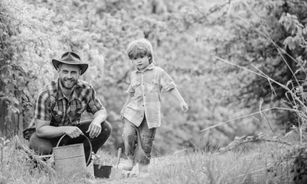 Tag der glücklichen Erde. Stammbaumschulen. Öko-Bauernhof. Kleinkind hilft Vater in der Landwirtschaft. Gießkanne, Topf und Hacke. Gartengeräte. Vater und Sohn mit Cowboyhut auf der Ranch. Fröhlicher Prozess — Stockfoto