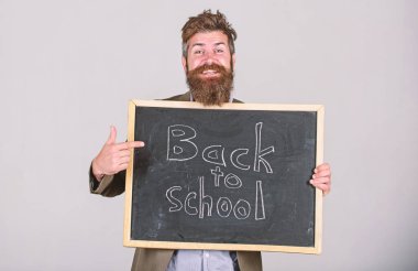 Invite to celebrate day of knowledge. Teacher bearded man stands and holds blackboard with inscription back to school grey background. Teacher advertises back to studying, begin school year