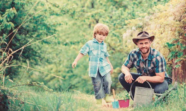 Happy Earth Day. Släktträd nursering. Eco Farm. liten pojke barn hjälpa pappa i jordbruket. Vattning kan, Pot och hacka. Trädgårdsutrustning. far och son i cowboyhatt på Ranch. Glädjefull process — Stockfoto