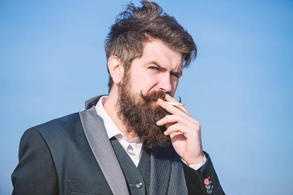 Taking a break to smoke. Bearded man smoking cigarette. smoke. brutal caucasian hipster with moustache. Future success. Male formal fashion. Businessman against the sky. Mature hipster with beard