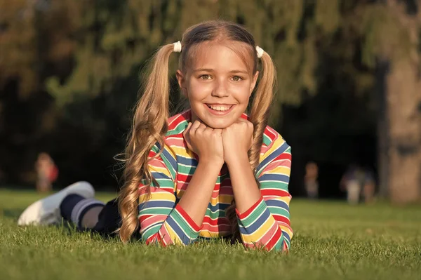 Cheerful schoolgirl on sunny day. Girl ponytails hairstyle enjoy relax. Living happy life. Happy smiling pupil. Have fun. Girl kid laying green grass. Healthy emotional happy kid relaxing outdoors — Stock Photo, Image