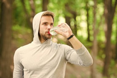 Susuz kalmamak. Sporcu parktaki eğitimden sonra su içer. Vücut sıvısına dikkat et. Spor ve sağlık. Kapüşonlu adam su içiyor. Antrenmandan sonra vitamin içeceği. Su şişeli atletik adam.