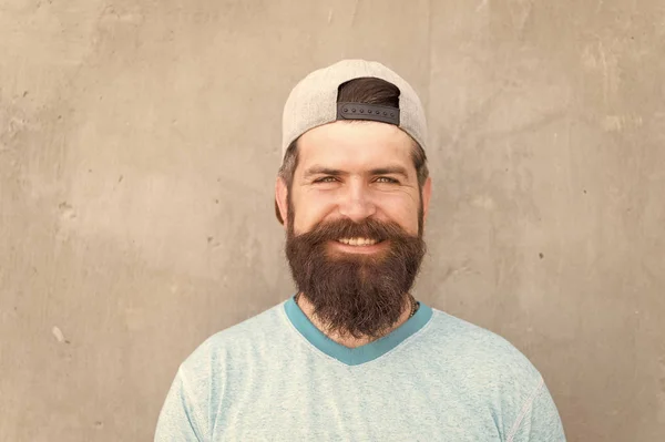 A barba separa os rapazes dos homens. Um caucasiano feliz a usar barba na parede cinzenta. Homem barbudo sorrindo com bigode elegante e forma de barba. Unshaven hipster com cabelo de barba texturizado ao ar livre — Fotografia de Stock