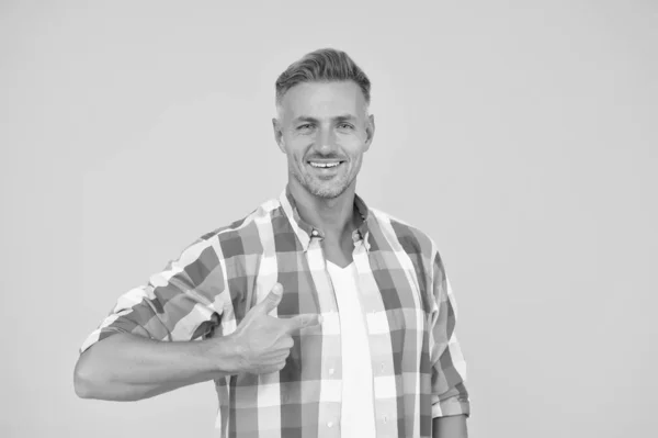 De beste winkels hier. Een volwassen man met een baard. Glimlachende man met de vinger, kopieerruimte. mannelijk model hemd. presentatie van het product. goederen voor mannen. Zomer verkoop hier. sexy man gele achtergrond — Stockfoto