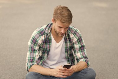 Dijital teknolojiler. Yakışıklı, kareli gömlek. Erkek modası. Öğrenci sakin ol, telefonu kullan. Adam dışarıda sohbet ediyor. Sokak tarzı. Adam yere oturur. Kaygısız öğrenci. Boş zaman harcamak. yaz modası