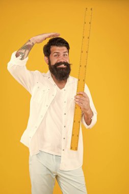 Cetvel ile yüksekliğini ölçüyor. Okul öğretmeni veya üniversite öğrencisi sarı arka plan üzerinde cetvel tutan. Sakallı adam metrik cetvel ile ölçüm alıyor. Benim cetvelim seninkinden daha uzun.