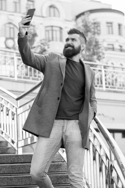 Ручное селфи. Бородатый мужчина делает селфи со смартфоном на открытом воздухе. Бизнесмен улыбается селфи-камере в мобильном телефоне. Наслаждаюсь селфи-сессией в деловом стиле. Современная жизнь — стоковое фото