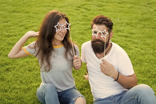 Festa de cabine de fotos para os amantes. Casal romântico sorrindo com feliz festa olhar na grama verde. Feliz namorada e namorado segurando adereços de festa no pau. Desfrutando de diversão festa — Fotografia de Stock