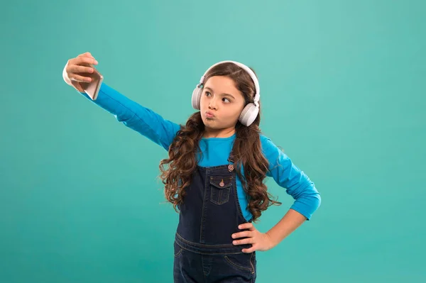 Ποζάρω για φωτογραφία. Ένα παιδί με σέλφι και ακουστικά. μικρό παιδί βιντεοκλήση στο smartphone. μικρό κορίτσι κρατήσει το κινητό τηλέφωνο. blogging στη σύγχρονη ζωή. Μαθήτρια χρησιμοποιεί νέα τεχνολογία. ζουν σε εικονικό κόσμο — Φωτογραφία Αρχείου