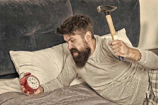 Doente e cansado. Um tipo irritado destrói um relógio irritante. O homem acordou infeliz com o despertador a tocar. Dorme mais. Conceito de sono saudável. Homem barbudo hipster quer dormir. ruído de ódio de despertador — Fotografia de Stock